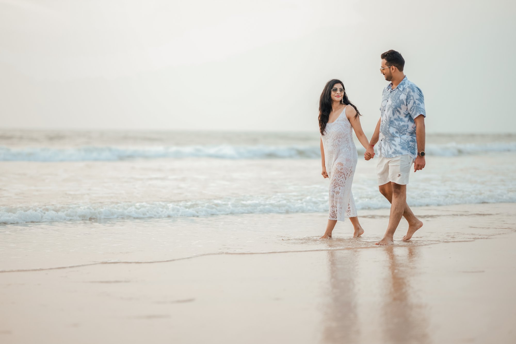 Beach romance unfolds as a couple holds hands and smiles at each other.